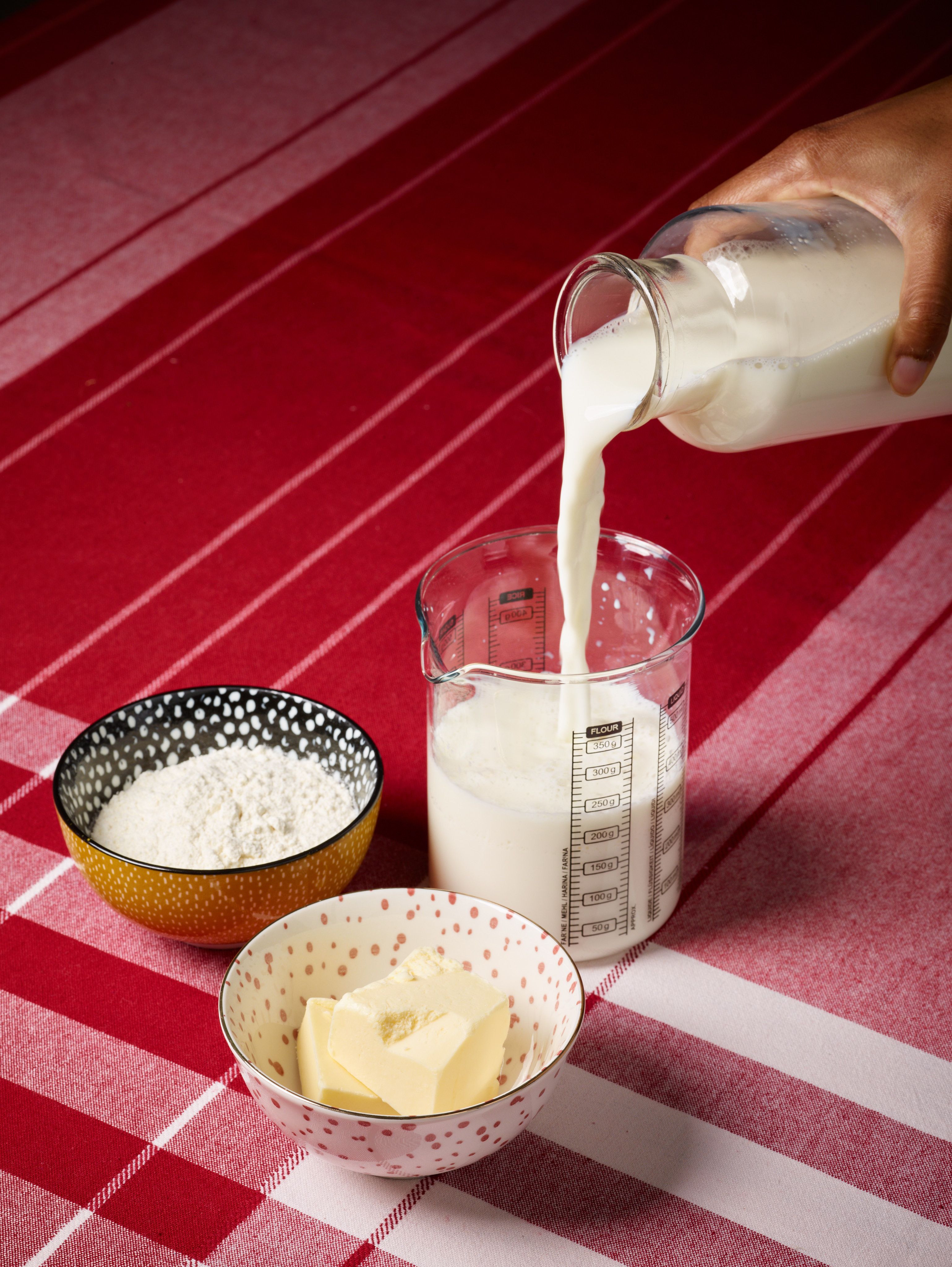 Milk being poured into a measuring cup next to bowls containing flour and butter